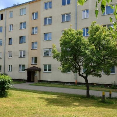 Blok mieszkalny z zielenią przed budynkiem, idealny na remont starego mieszkania.